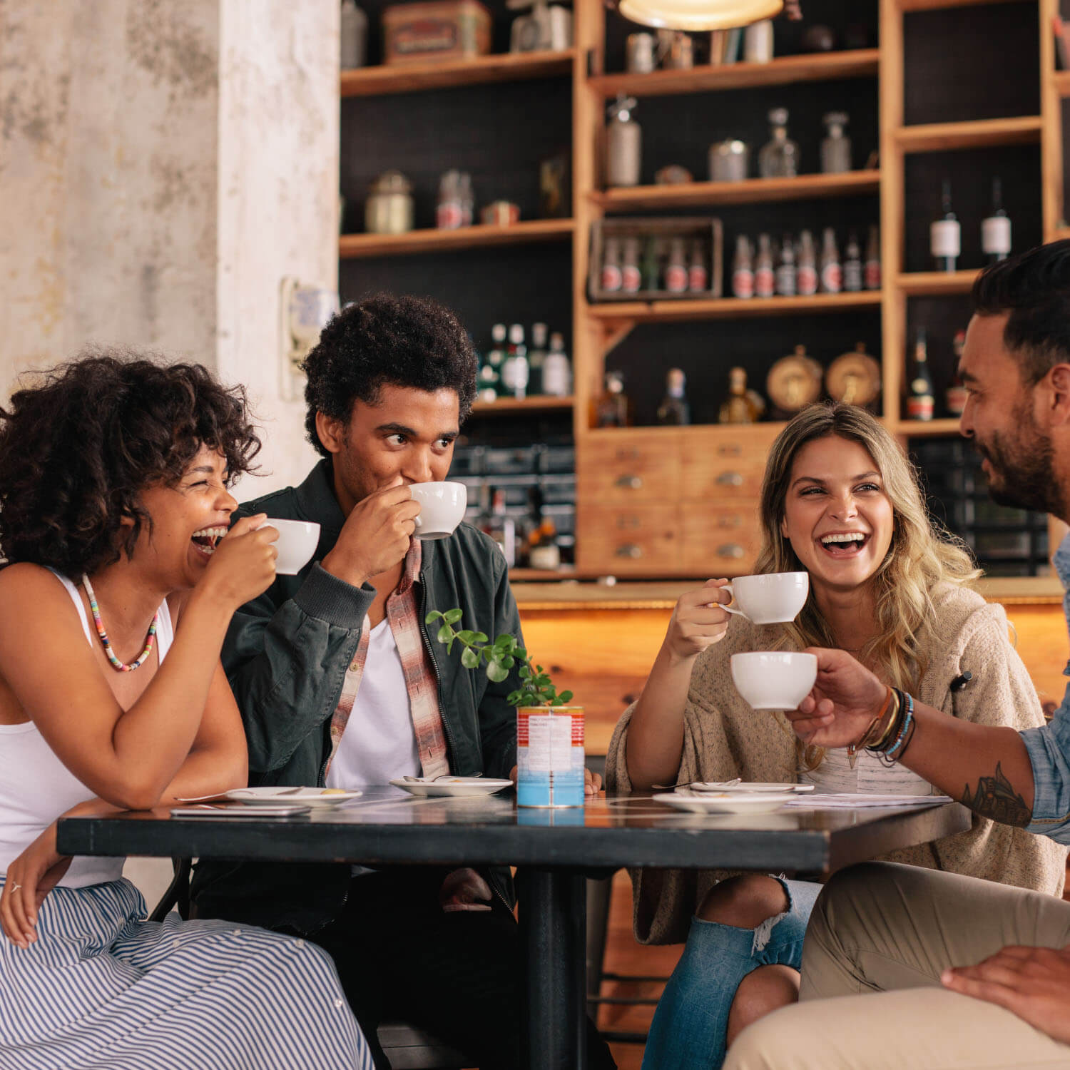 Imagen de un grupo de cuatro adultos jóvenes tomando café y hablando en una cafetería