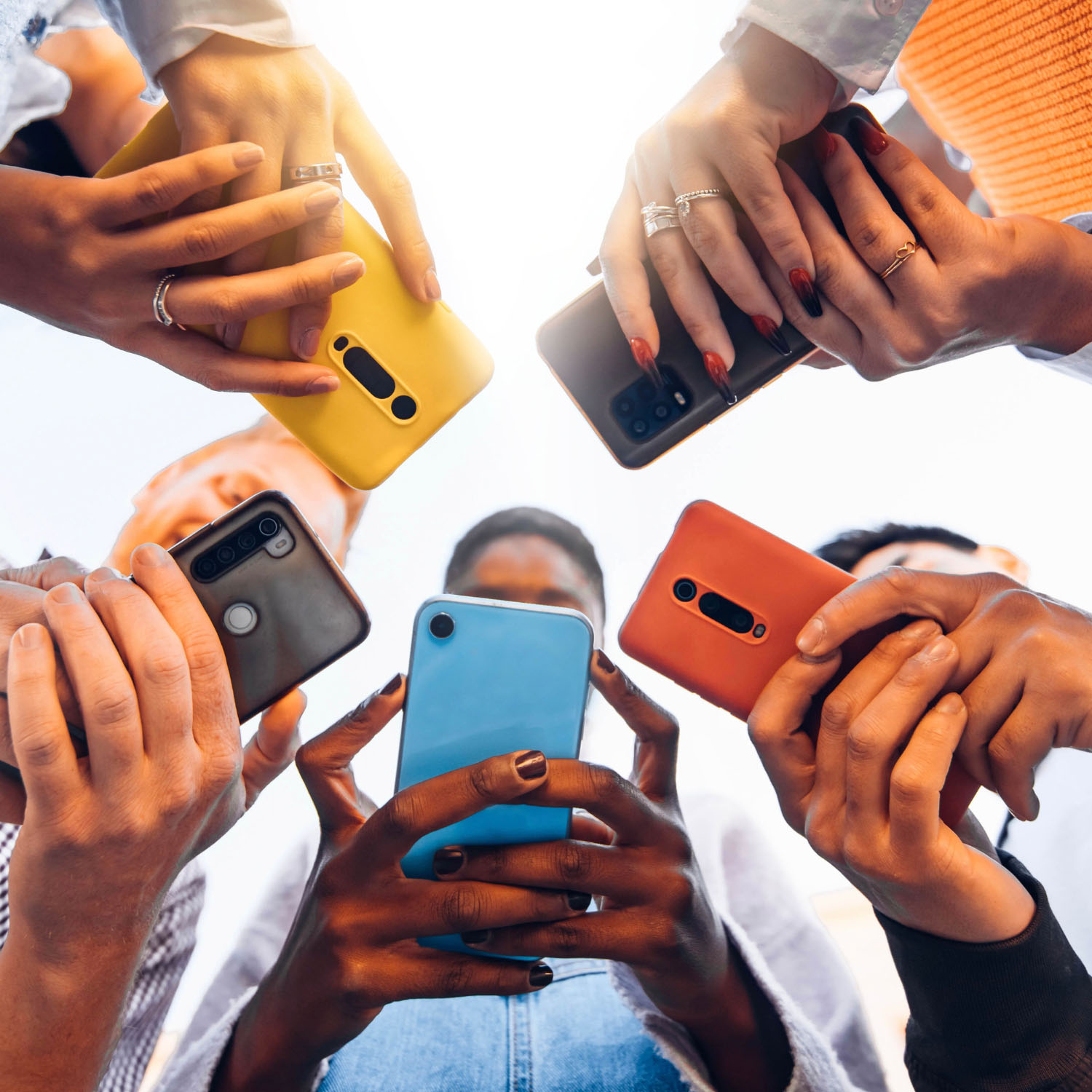 Un grupo de cinco adolescentes formando un círculo mientras sostienen sus celulares y miran las pantallas.